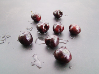 A pool of water.Fresh black cherries lined up on a black gray background