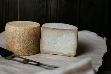 Hard cheese kravot or parmesan on a wooden dark board. Cheese knife next to the cheese heads