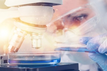 Female scientist in mask and glasses working with microscope