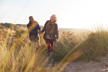 Loving Active Senior Couple Holding Hands As They Walk Through Sand Dunes