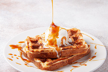 Belgian waffles with ice cream and splashing caramel on a white plate. Homemade waffer craft...