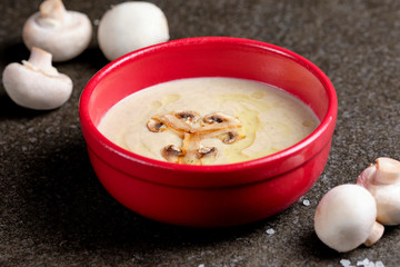 Bowl of mushroom cream soup with fried champignon mushrooms and vegetables on black stone background. Rustic style. Close up.