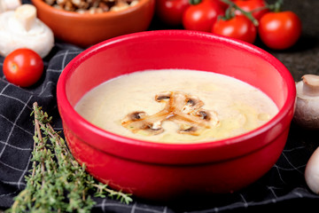 Bowl of mushroom cream soup with fried champignon mushrooms and vegetables on black stone background. Rustic style. Close up.