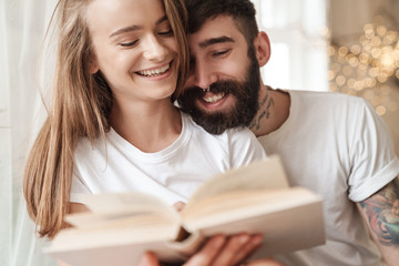 Image of happy young couple laughing and reading book while sitting