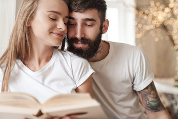 Image of happy young couple smiling and reading book while sitting