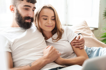 Image of caucasian concentrated couple using laptop and hugging