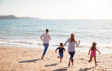 Rear View Of Family On Beach Running Across Sand Towards Sea