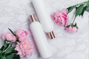 Peonies and white cosmetic bottles on a marble background