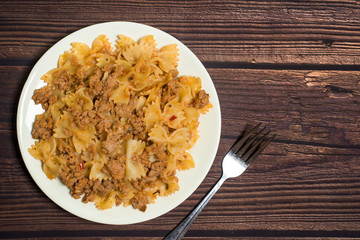 pasta with meat on a wooden background with a fork in hand. photo for banner, place for text