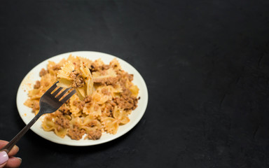 pasta with meat on a dark background. on a fork, pasta in the shape of a butterfly with meat . the view from the top. space for text. photo for banner