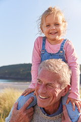 Grandfather Giving Granddaughter Ride On Shoulders As They Walk Through Sand Dunes