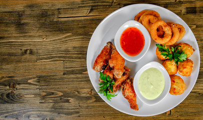snacks to beer. cheese balls, chicken wings, onion rings, sauce on a wooden background. with copy space. top view