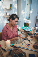 Vertical image of a young female  artist working in a workshop, attractive woman jeweler creates a new collection of earrings, Handmade Art Hobby Artisan Jewelry