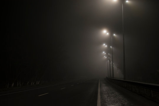 Empty Road Fog At Night. Along The Road Lights Are On.