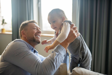 Obraz premium Bearded man smiling while holding his baby daughter