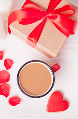 Cup of coffee and a heart shaped red cookie with gift box on the white table