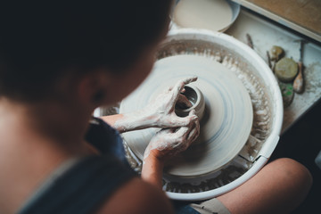 Back view of a young woman working with clay in pottery studio, Professional female potter making vase on a pottery wheel