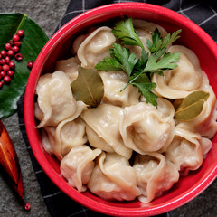 Russian pelmeni meat with butter, chili pepper, branch of cherry tomatoes, fresh vegetables, herbs on black stone background. Bowl with tasty dumplings and bay leaf. Rustic style.