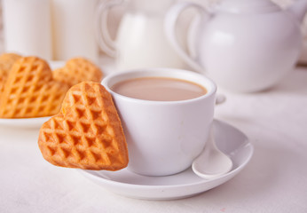 Cup of coffee and a heart shaped cookies on the white table
