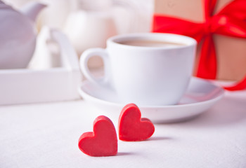Fototapeta na wymiar Cup of coffee and a heart shaped red chocolate candies with gift box on the white table