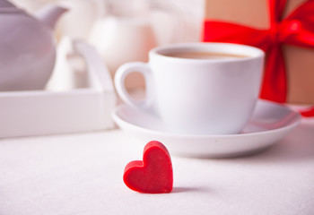 Obraz na płótnie Canvas Cup of coffee and a heart shaped red chocolate candy with gift box on the white table
