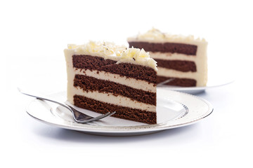 Two homemade cocoa sponge cakes with sugar mass on a plate with a fork on a white background.