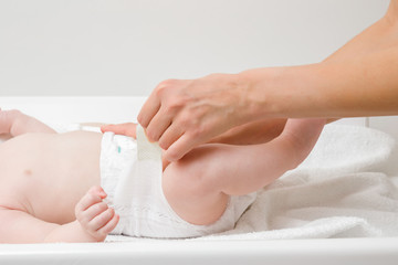 Young mother hands changing diaper for baby on white towel. Closeup. Side view.