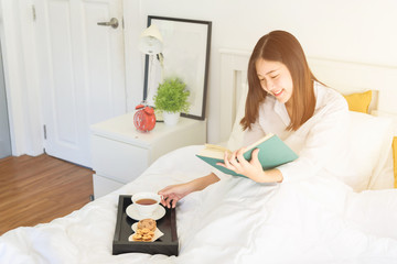 Relaxed young girl lying in bed, at her room enjoying reading a book. Rest and relax concept..