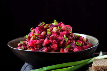 Vinaigrette salad with boiled vegetables in a clay bowl against the black background. Russian cuisine meal