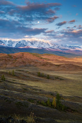 The moon over the North Chuysky ridge, dawn. Autumn in the Altai mountains. Russia