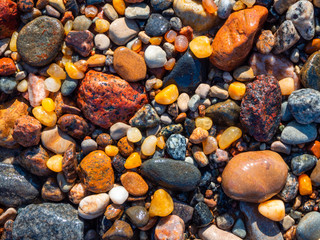 Small amber stone and pebbles on the sandy beach. Shallow wet amber washed by waves. Natural mineral at the Baltic sea coast.  Top view.