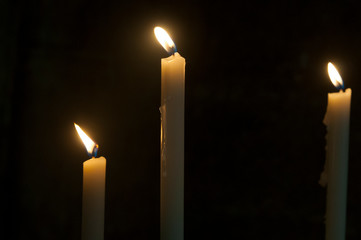 White wax candles burn on black background