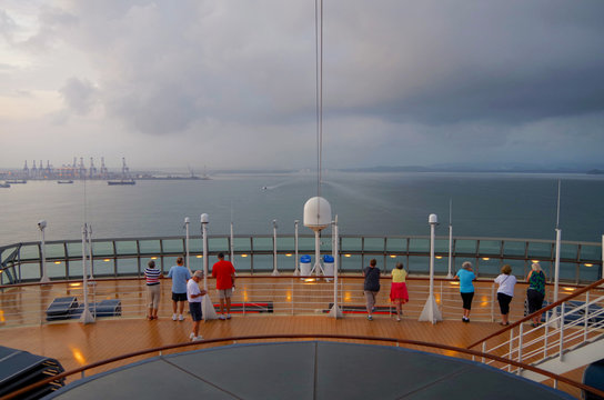 People watching cruiseship or cruise ship liner arrive to entry and first lock of Panama Canal from forward outdoor deck with industrial port in background during morning hours
