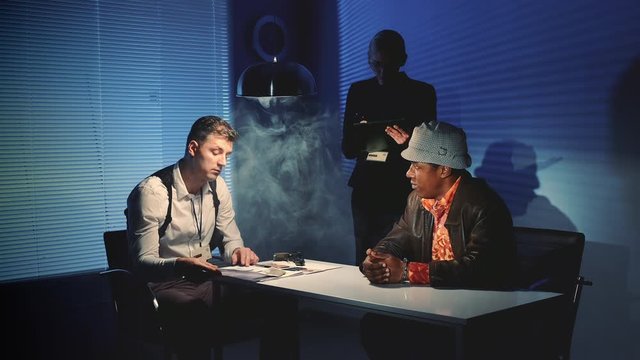 Multiracial offender grabbing the gun and threatening to harm detectives during interrogation process. They are very scared and raise their hands up.