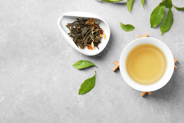 Cup of green tea, dry and fresh leaves on grey table, flat lay. Space for text
