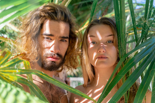 Portrait of naked young couple among palm leaves