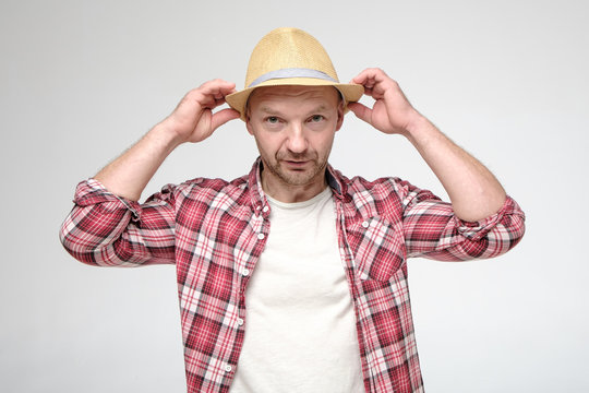 Caucasian Man Puts On Hat And Looks Uncertainly At The Camera.