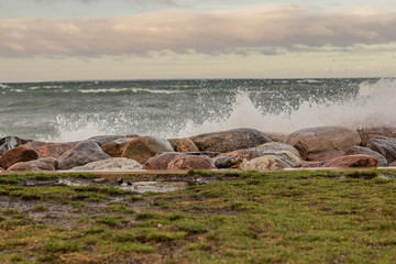 Wet stones with a stormy sea in the background with waves and wet grass in the foreground
