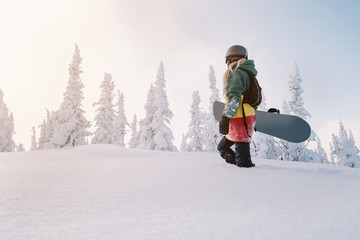 Fototapeta na wymiar Female snowboarder wearing long dreadlocks and ratsa hoody in white winter forest walking in snow powder