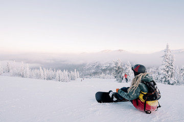 Fototapeta na wymiar sitting female snowboarder wearing long hair preparing for riding from mountain top