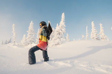 young adult female snowboarder standing with snowboard behind winter forest
