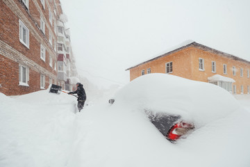 Heavy snowfall. People trying to clear snow-covered cars parked near houses in winter city
