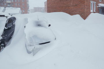 Heavy snowfall. snow covered cars  in a snowdrift near houses in winter city