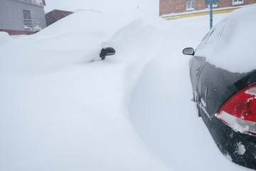 Heavy snowfall. snow covered cars  in a snowdrift near houses in winter city