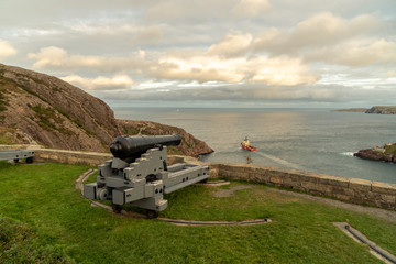 A modern deep water drilling rig support ship going out to sea under the watchful old cannon from the Queen's Battery #3, St. John's, Newfoundland