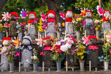 Rows jizo statues with red bibs, hats, flower and colorful wind mills at Zojoji temple in Tokyo,...