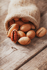Pecans are spilled out of a burlap bag onto a wooden table in close-up.