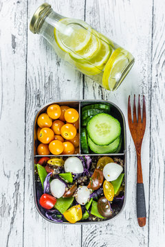 Bottle of lemonade and lunchbox with cucumber slices, winter cherries and quinoa salad (quinoa, cherry tomato, red cabbage, sugar snap peas and mozzarella Balls)