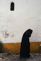 Black hooded monk wearing long cloak walking on middle ages European street