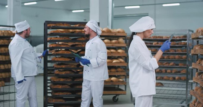Bakery industry large video taking three bakers chatting with each other tone pretty lady baker in a white uniform taking photos of a fresh baked bread